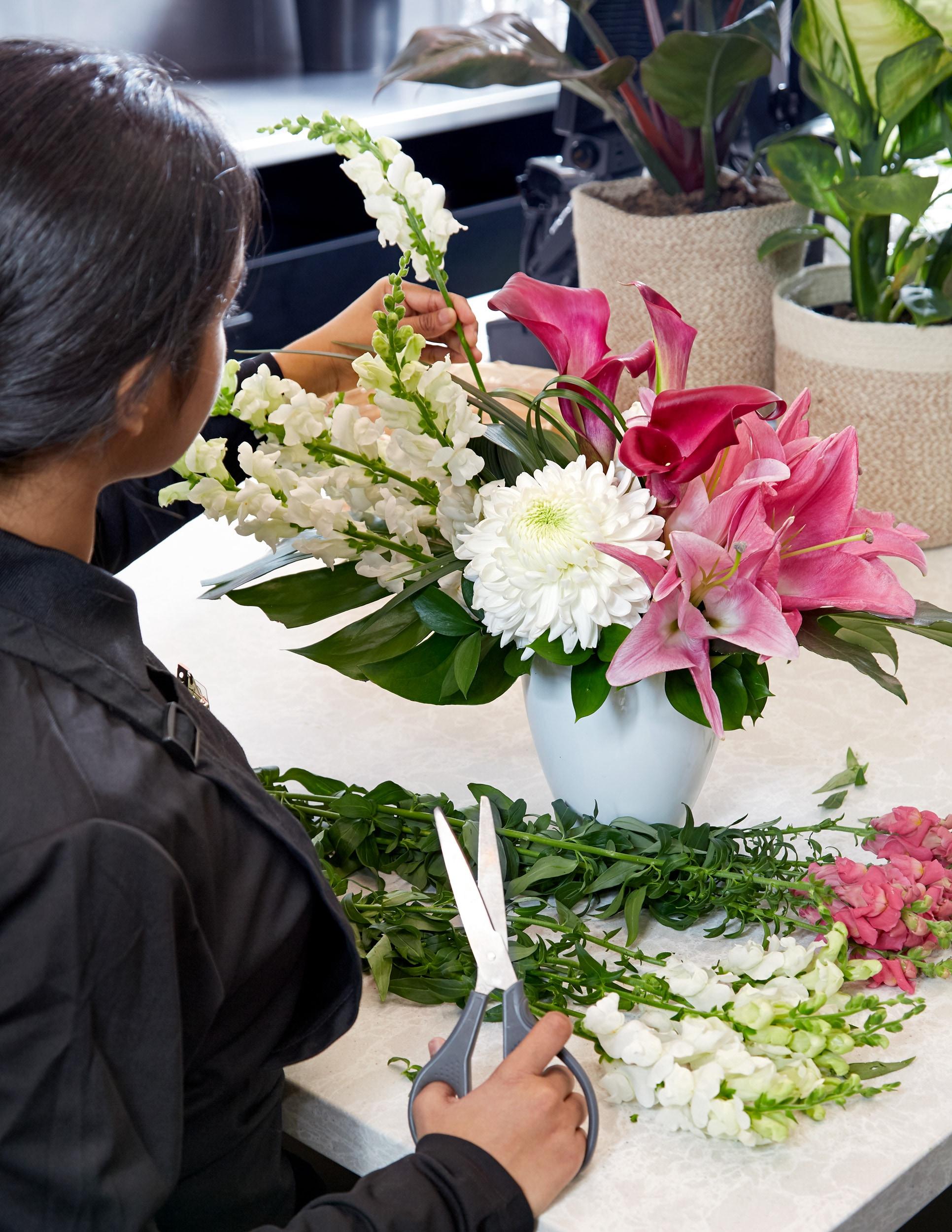 A Flowers by Fortinos floral designer creates an arrangement with pink lillies, white snapdragons and greens.