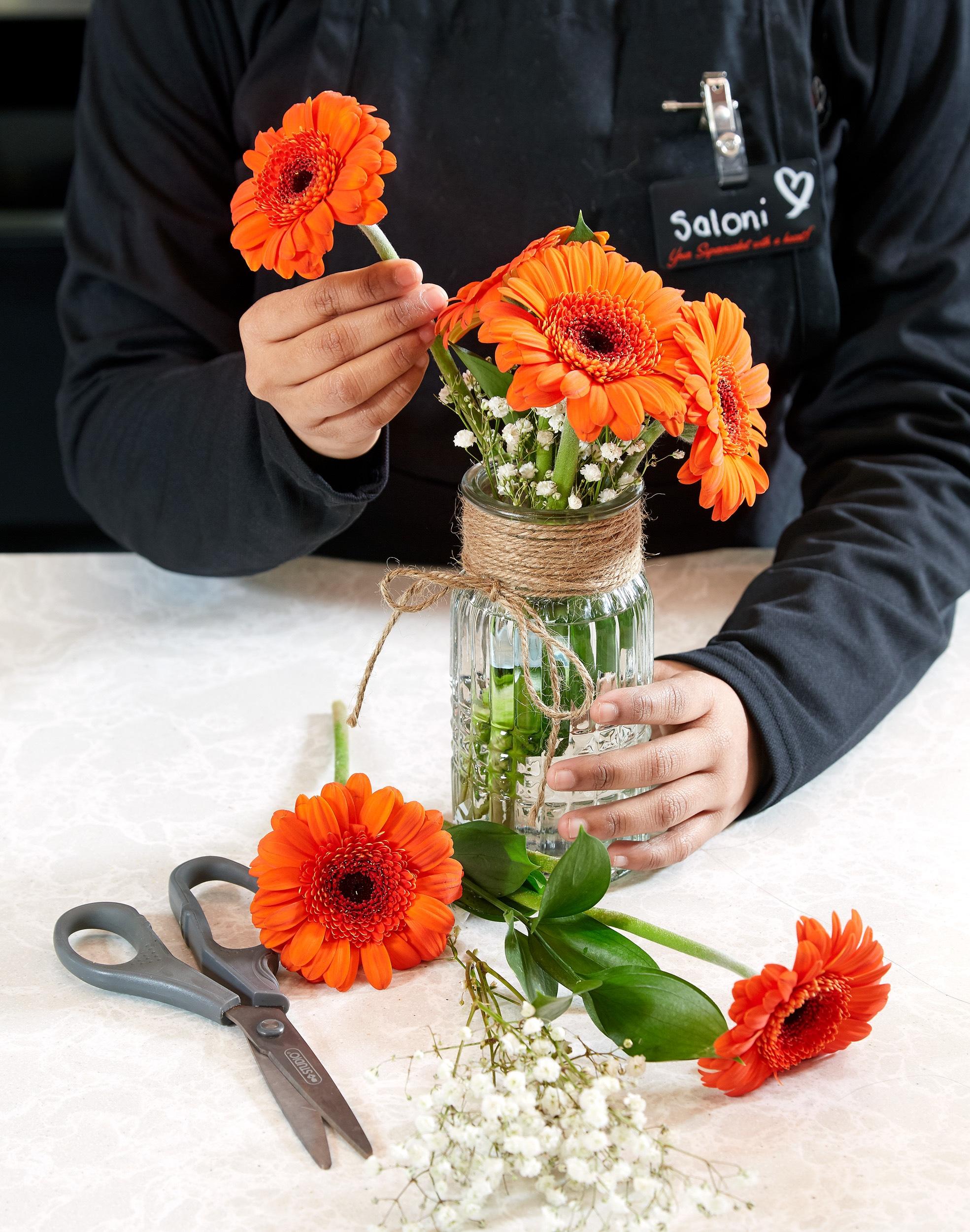 A Flowers by Fortinos floral designer placing orange gerberas into a vase.